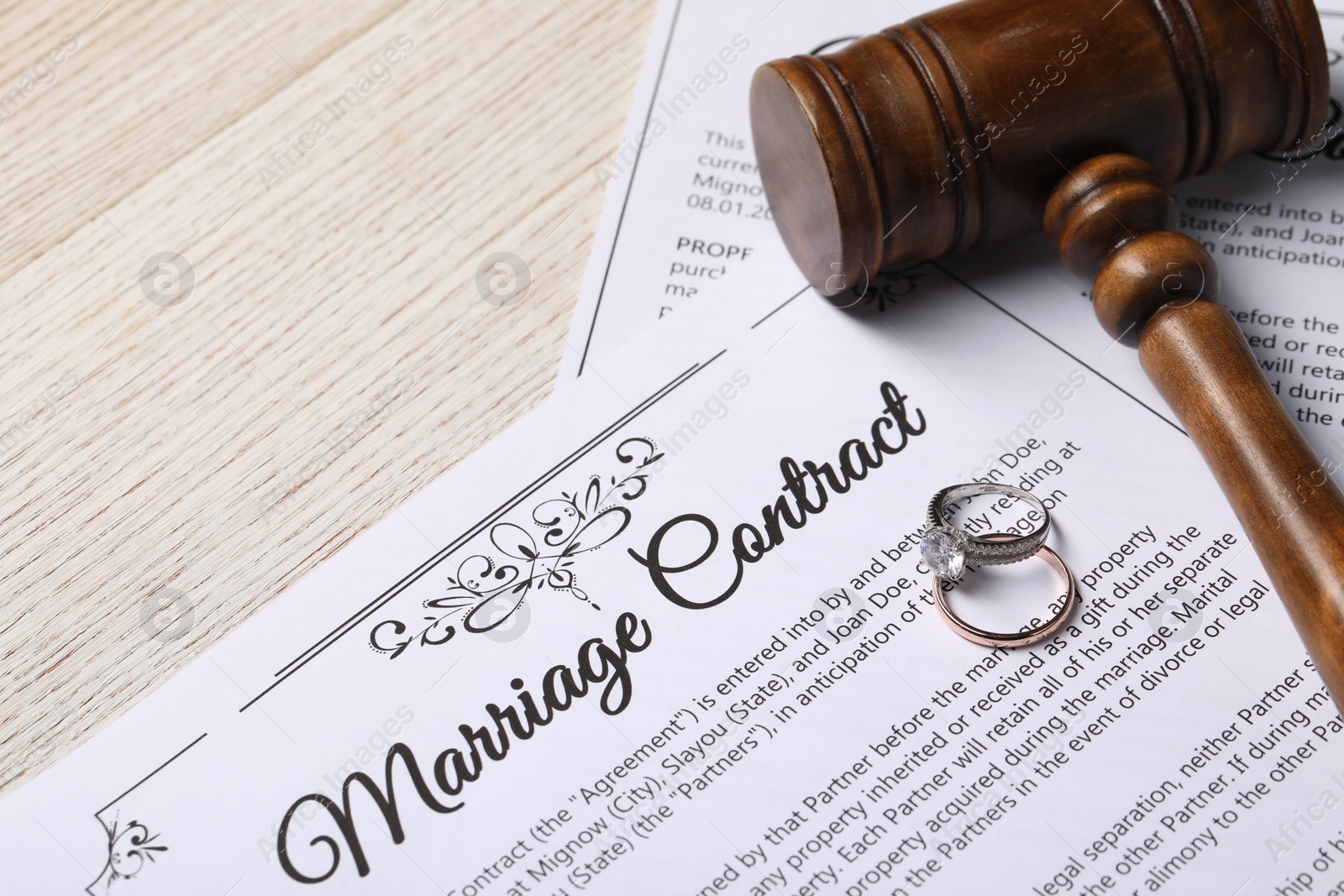 Photo of Marriage contract, wedding rings and gavel on wooden table, closeup