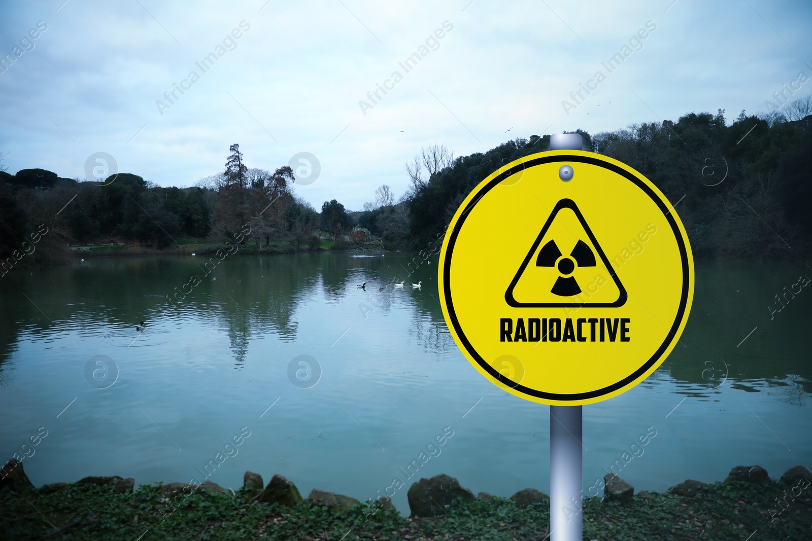 Image of Radioactive pollution. Yellow warning sign with hazard symbol near lake