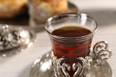 Photo of Glass of traditional Turkish tea in vintage holder on table, closeup
