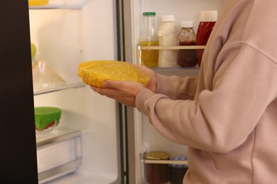 Photo of Man putting bowl covered with beeswax food wrap into refrigerator, closeup