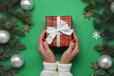 Woman holding gift box near fir tree branches with Christmas decor on green background, top view