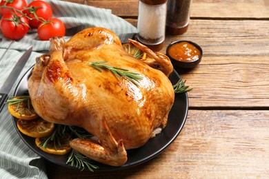 Photo of Tasty roasted chicken with rosemary, sauce and lemon on wooden table, space for text