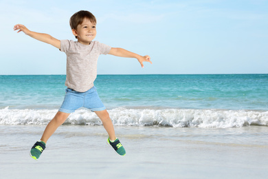 Image of Happy school boy jumping on beach near sea, space for text. Summer holidays