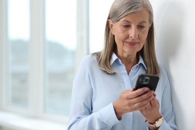 Photo of Senior woman using mobile phone at home, space for text