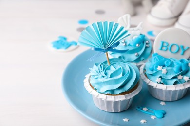 Photo of Delicious cupcakes with light blue cream and toppers for baby shower on white wooden table