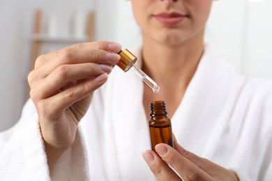 Woman with bottle of cosmetic serum and dropper on blurred background, closeup