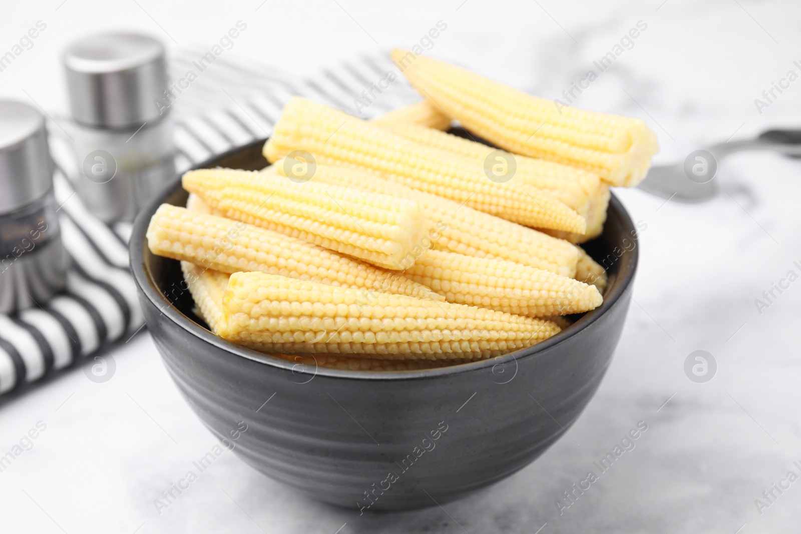 Photo of Bowl of pickled baby corn on white marble table, closeup