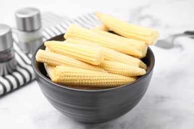 Bowl of pickled baby corn on white marble table, closeup