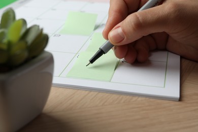 Photo of Timetable. Man making schedule using calendar and sticky note at wooden table, closeup