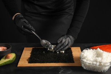 Chef in gloves making sushi roll at dark table, closeup