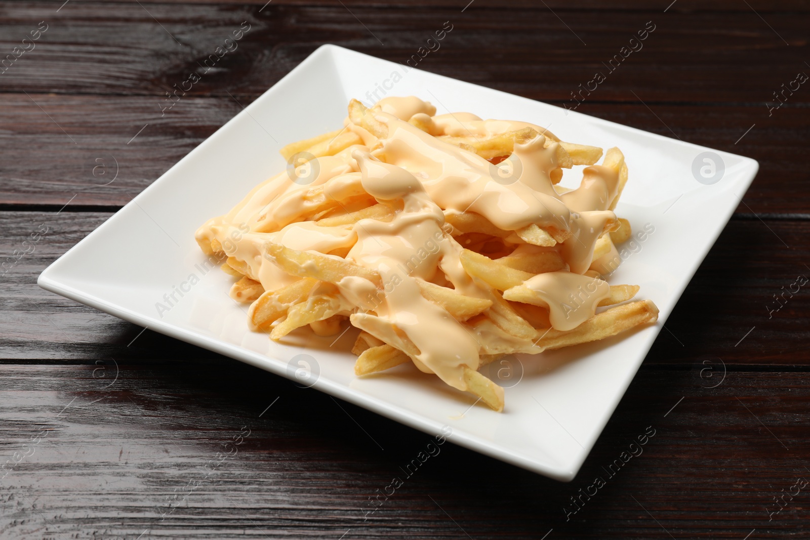 Photo of Delicious french fries with cheese sauce on wooden table