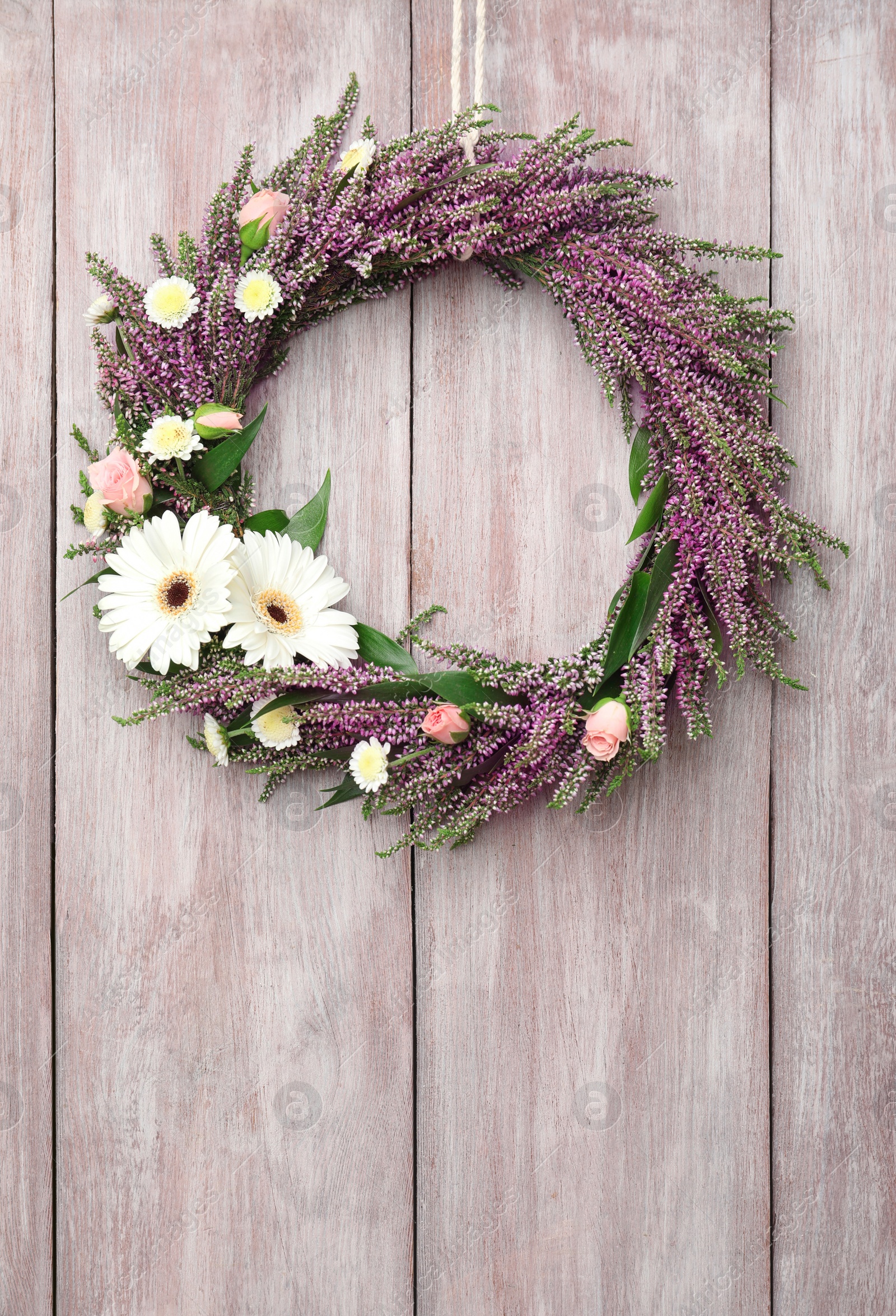 Photo of Beautiful autumnal wreath with heather flowers hanging on light wooden background. Space for text