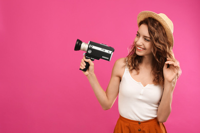 Beautiful young woman with vintage video camera on crimson background, space for text