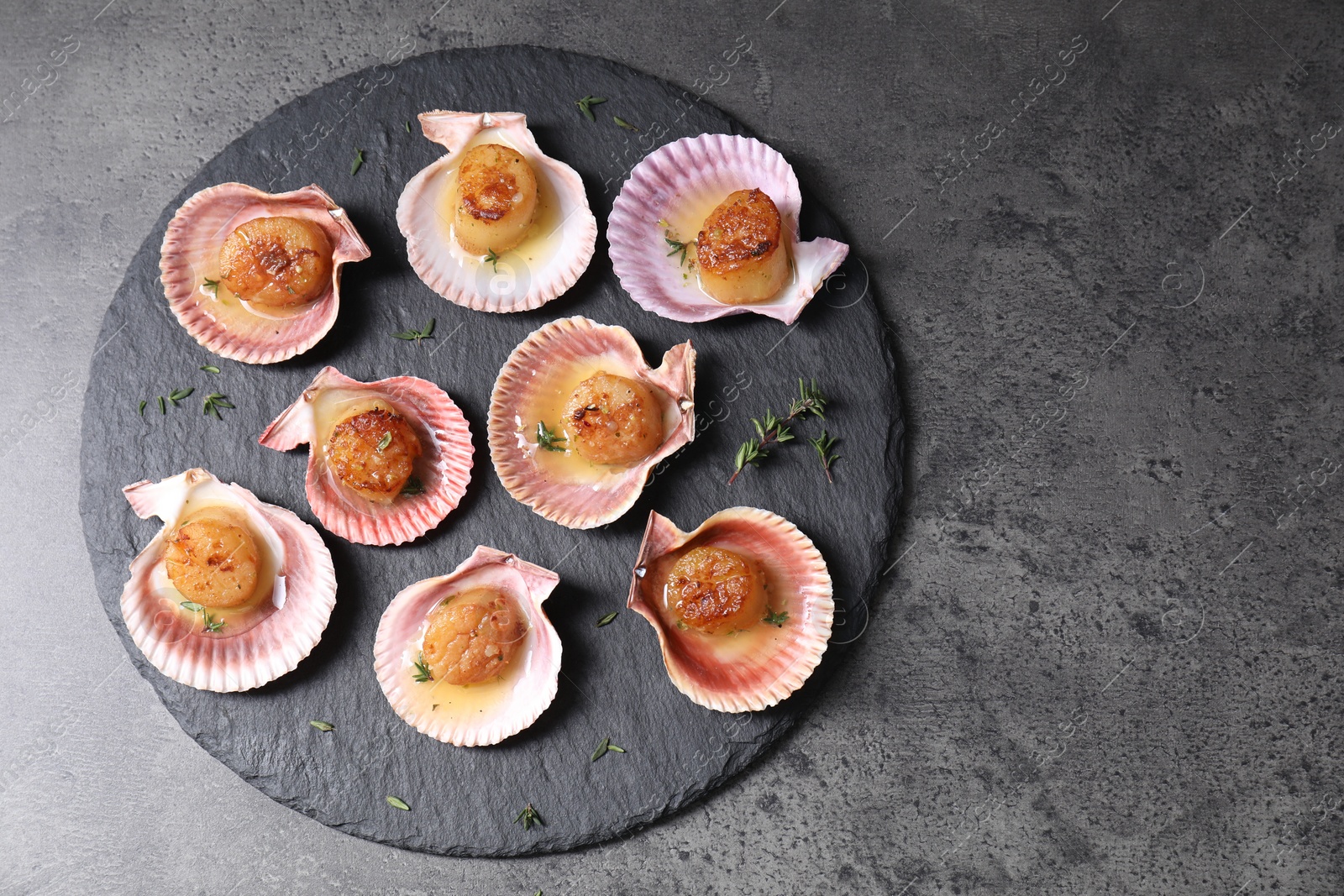 Photo of Delicious fried scallops in shells on grey table, top view. Space for text