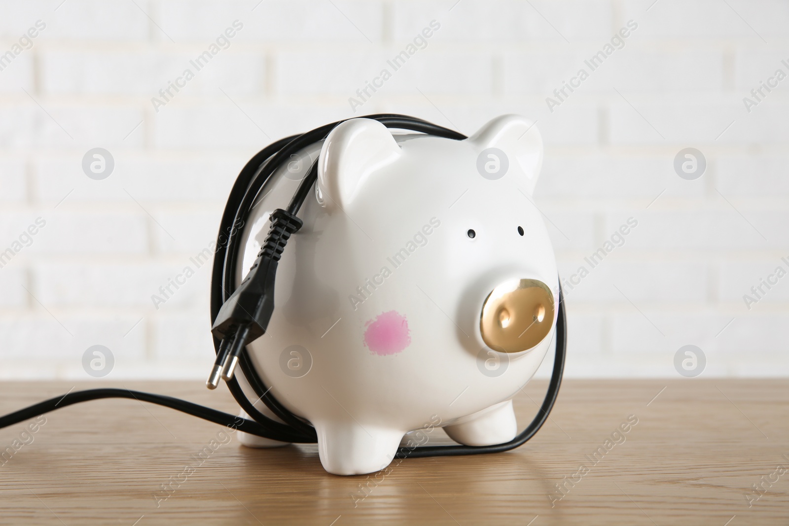 Photo of Piggy bank with power plug on wooden table. Energy saving concept