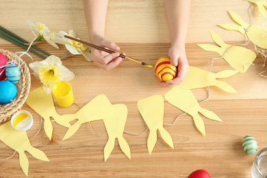 Photo of Little child painting Easter egg at wooden table, above view