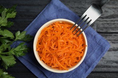 Photo of Delicious Korean carrot salad and parsley on black wooden table, flat lay