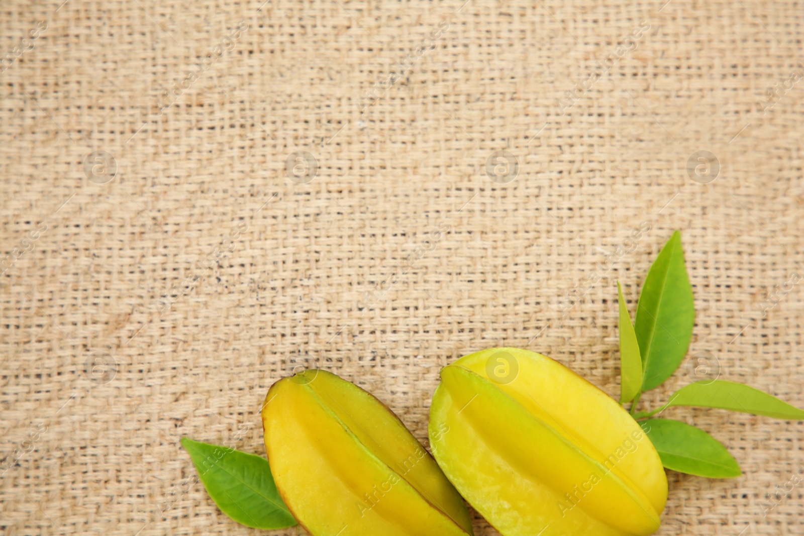 Photo of Delicious ripe carambolas with leaves on burlap fabric, flat lay. Space for text