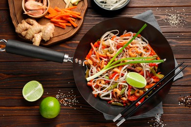 Photo of Shrimp stir fry with noodles and vegetables in wok on wooden table, flat lay