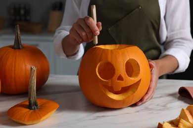 Photo of Woman carving pumpkin for Halloween at white marble table in kitchen, closeup