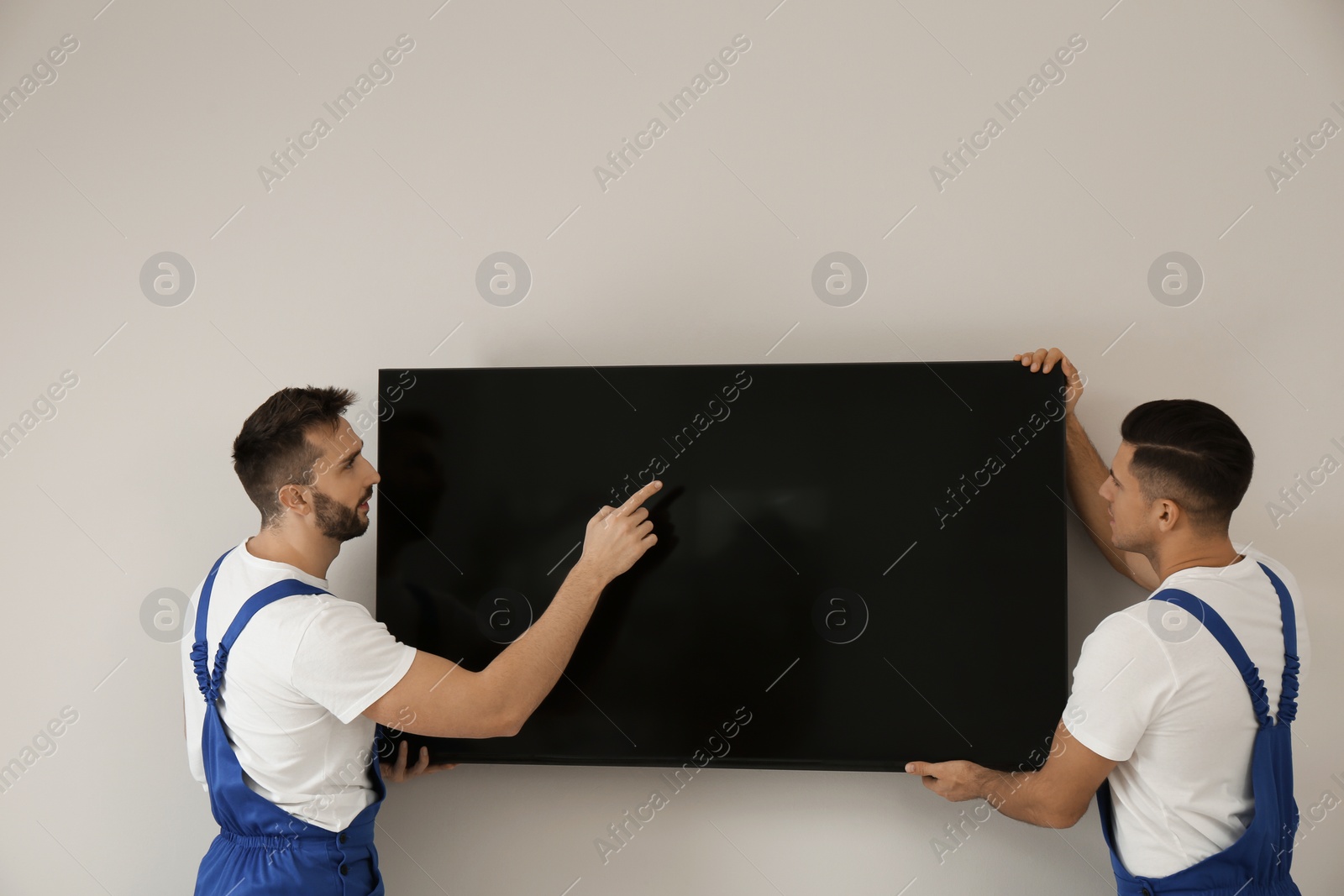 Photo of Professional technicians installing modern flat screen TV on wall indoors