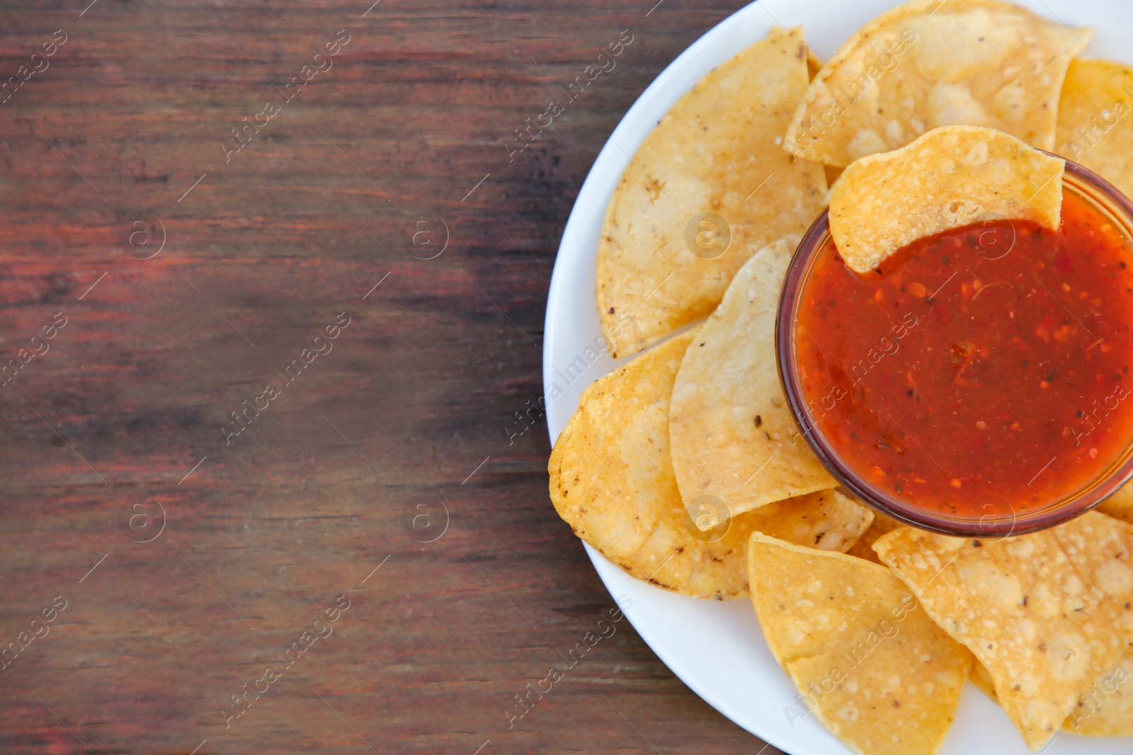 Photo of Tasty salsa sauce and tortilla chips on wooden table, top view. Space for text