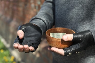 Photo of Poor homeless man holding bowl with donations outdoors, closeup