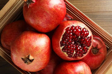 Photo of Ripe pomegranates in crate on wooden table, top view