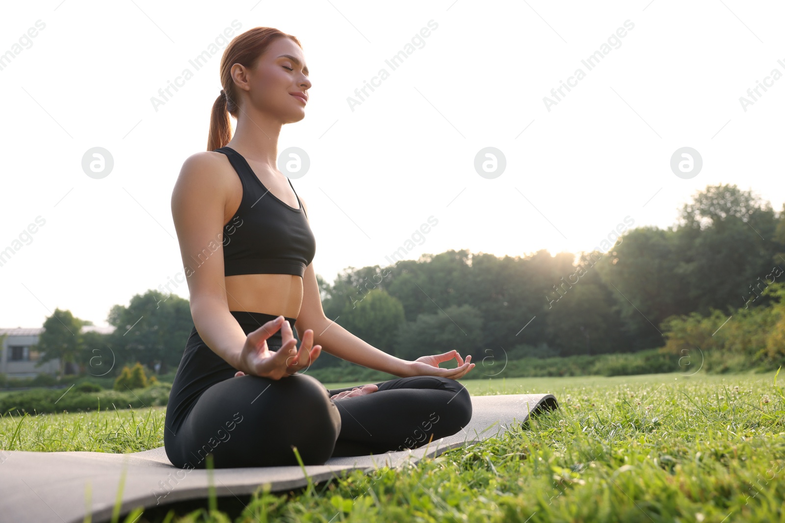 Photo of Beautiful young woman practicing Padmasana on yoga mat outdoors, low angle view and space for text. Lotus pose