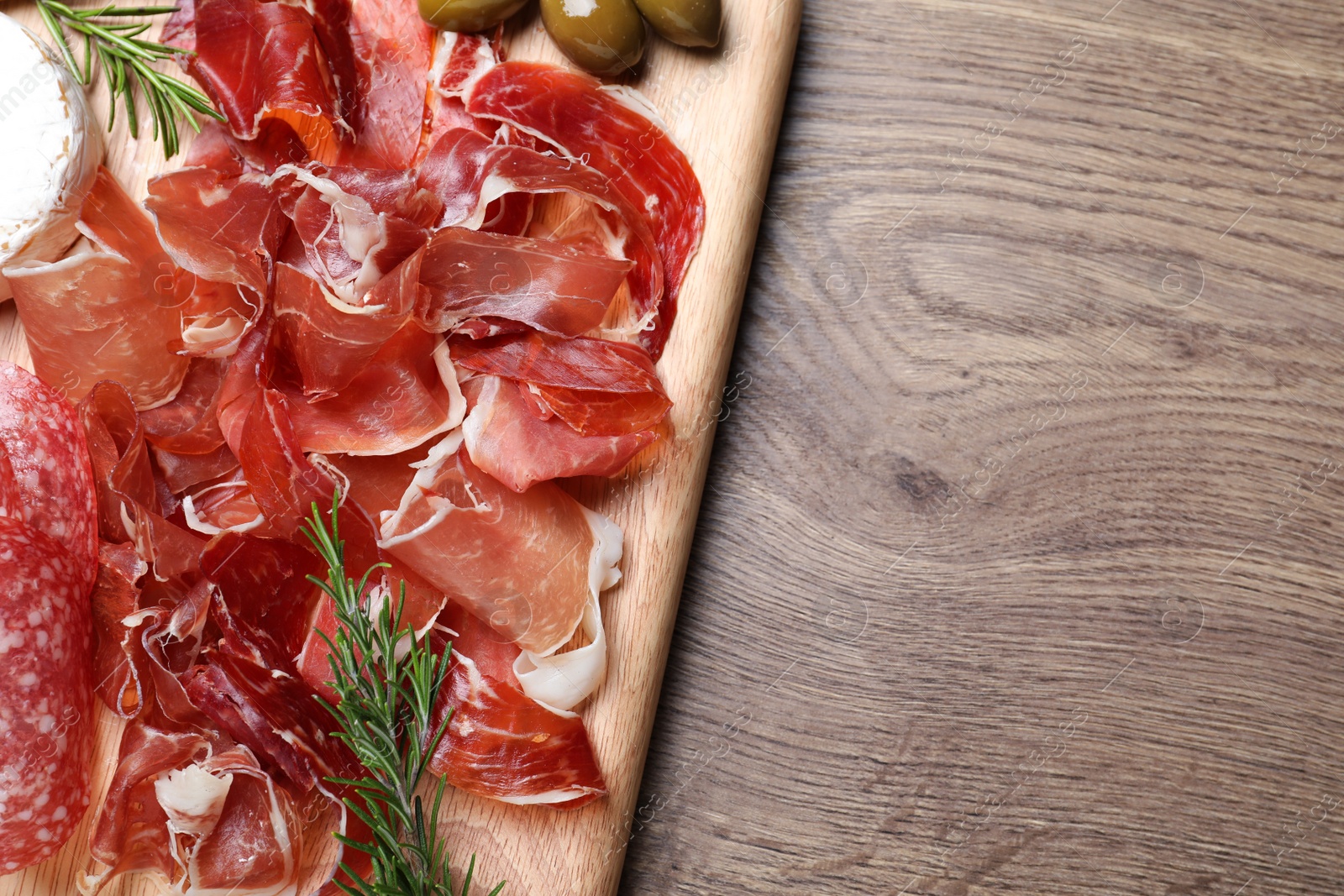 Photo of Tasty prosciutto served on wooden table, top view. Space for text