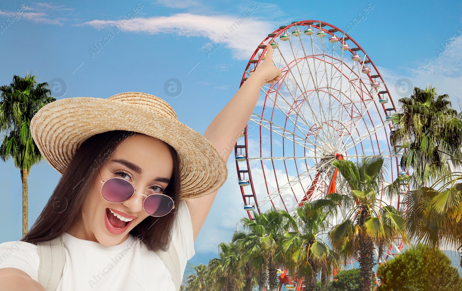 Image of Smiling young woman pointing at observation wheel while taking selfie outdoors