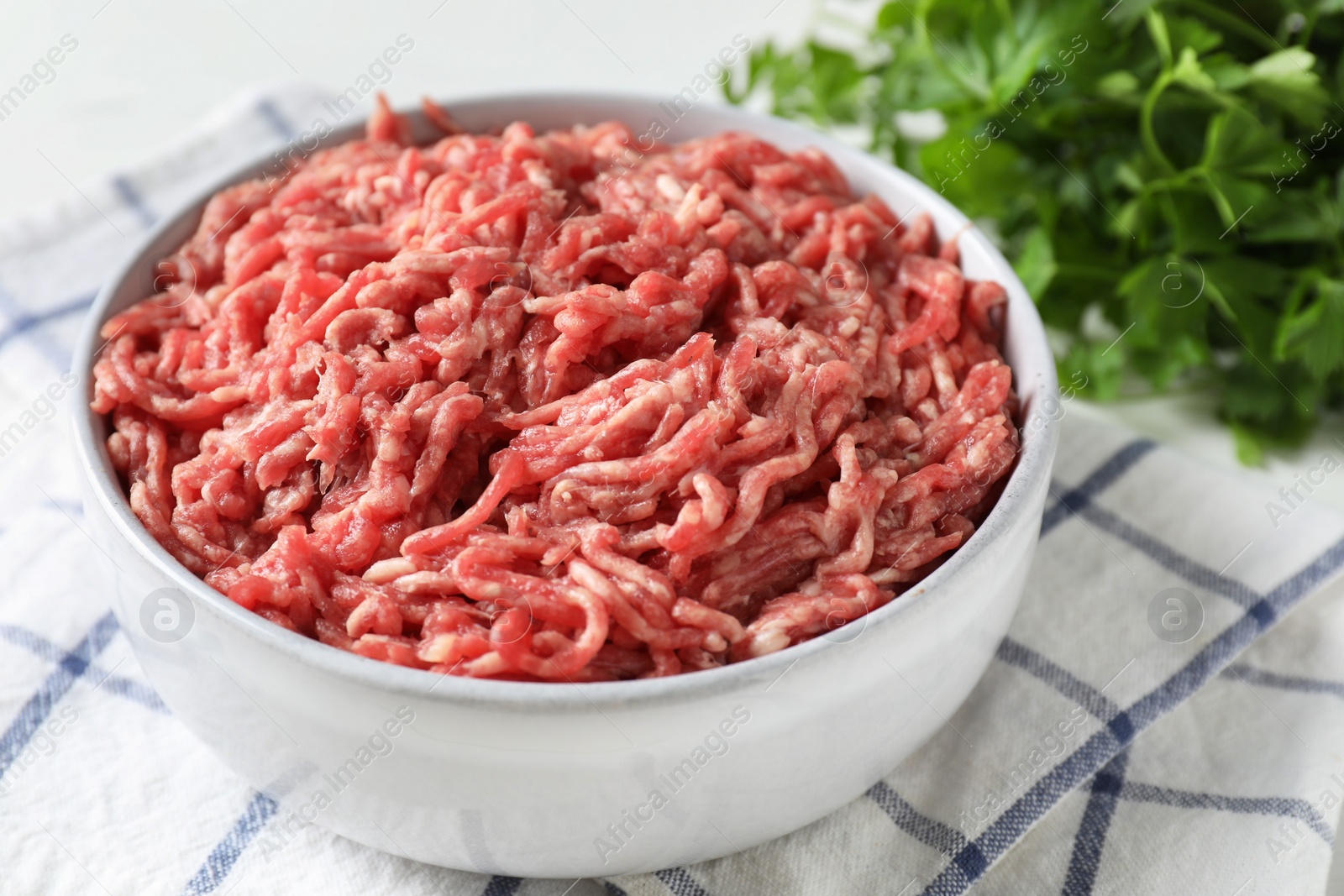 Photo of Raw ground meat in bowl and parsley on table, closeup