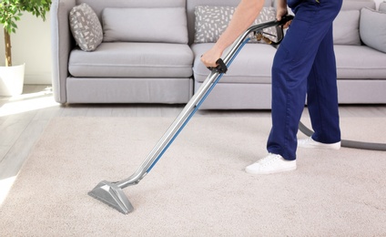 Photo of Male worker removing dirt from carpet with professional vacuum cleaner indoors