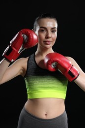 Portrait of beautiful woman in boxing gloves on black background