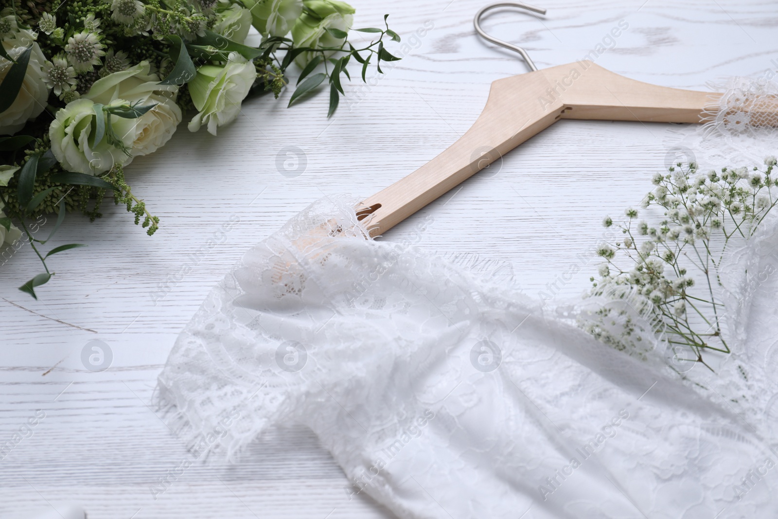 Photo of Beautiful wedding dress and flowers on white wooden background, closeup