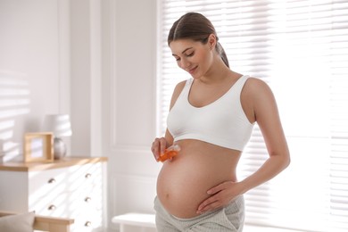 Photo of Young pregnant woman with cosmetic product at home