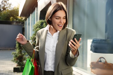 Special Promotion. Emotional young woman with shopping bags and smartphone near showcase