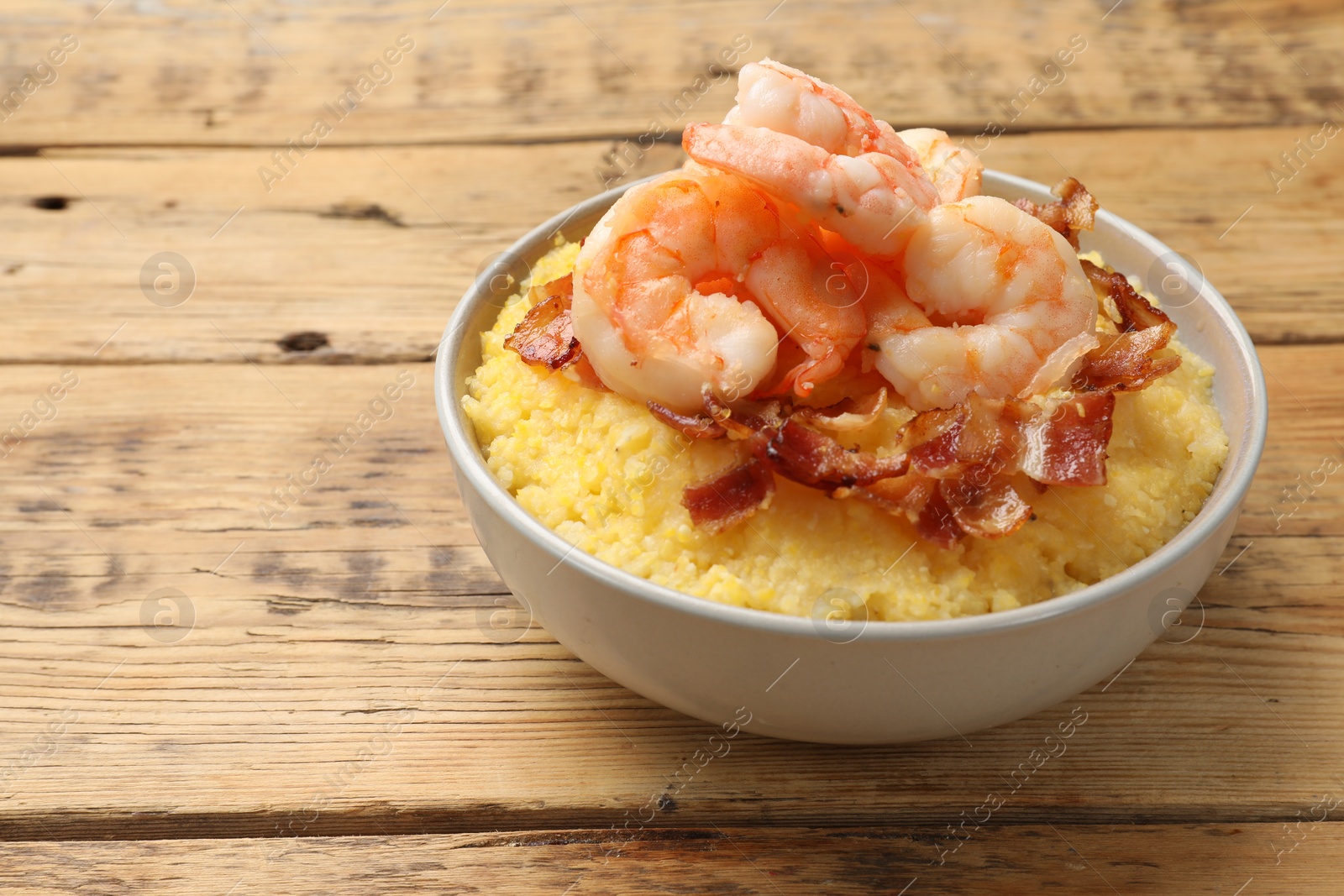 Photo of Fresh tasty shrimps, bacon and grits in bowl on wooden table, closeup. Space for text
