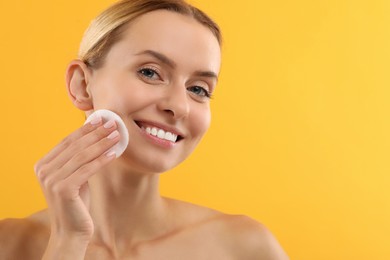Photo of Smiling woman removing makeup with cotton pad on yellow background, closeup. Space for text