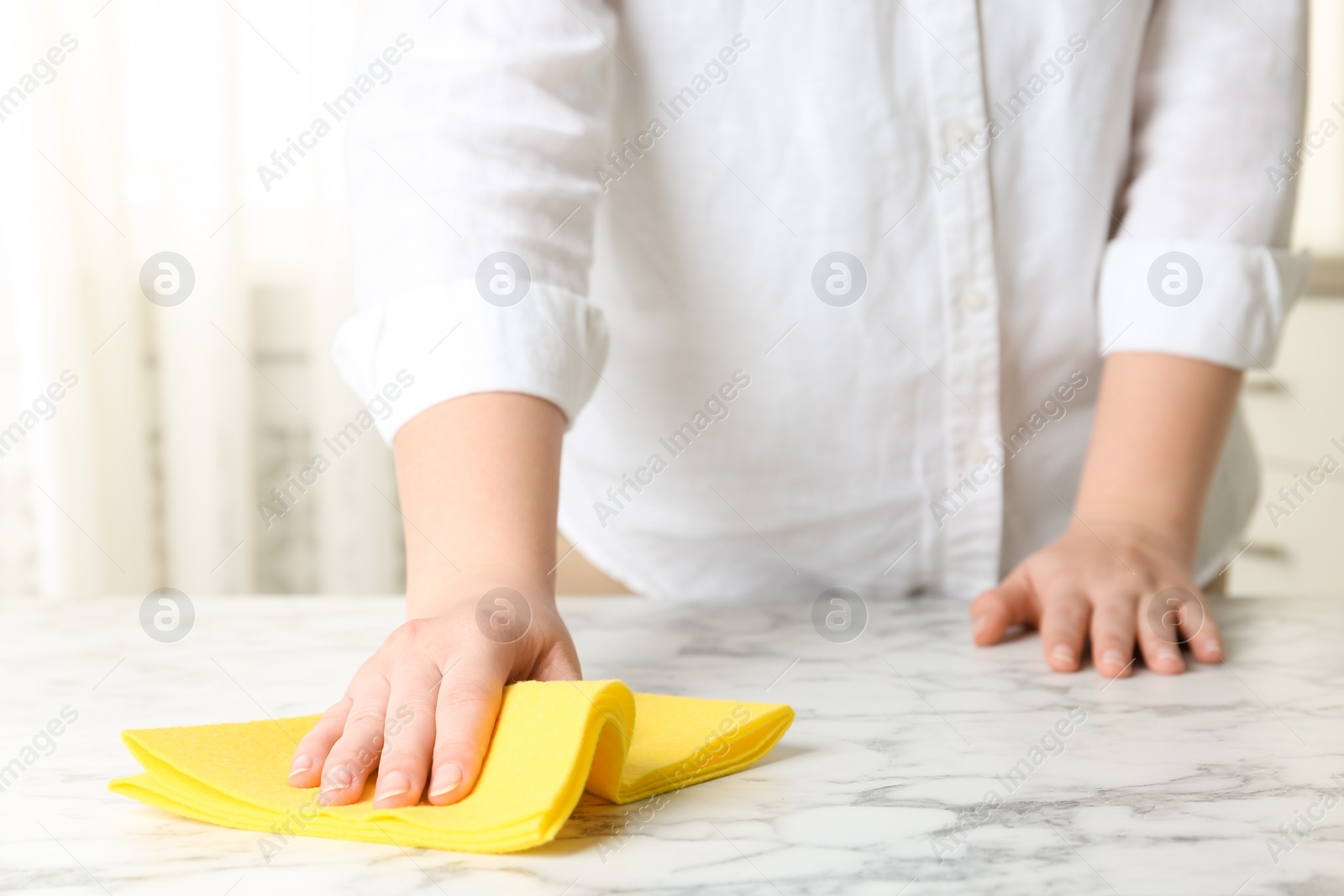 Photo of Woman wiping white marble table with rag indoors, closeup