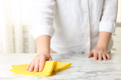 Photo of Woman wiping white marble table with rag indoors, closeup