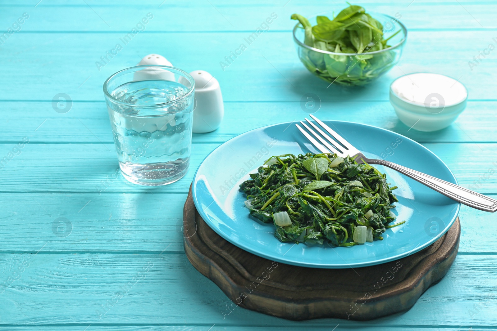 Photo of Tasty cooked spinach served on light blue wooden table. Healthy food