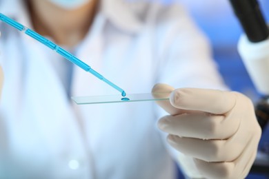 Photo of Scientist dripping sample of light blue liquid onto microscope slide in laboratory, closeup