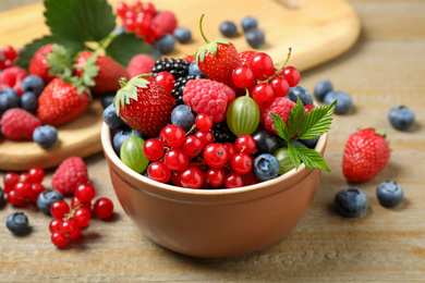 Mix of different fresh berries in bowl on wooden table