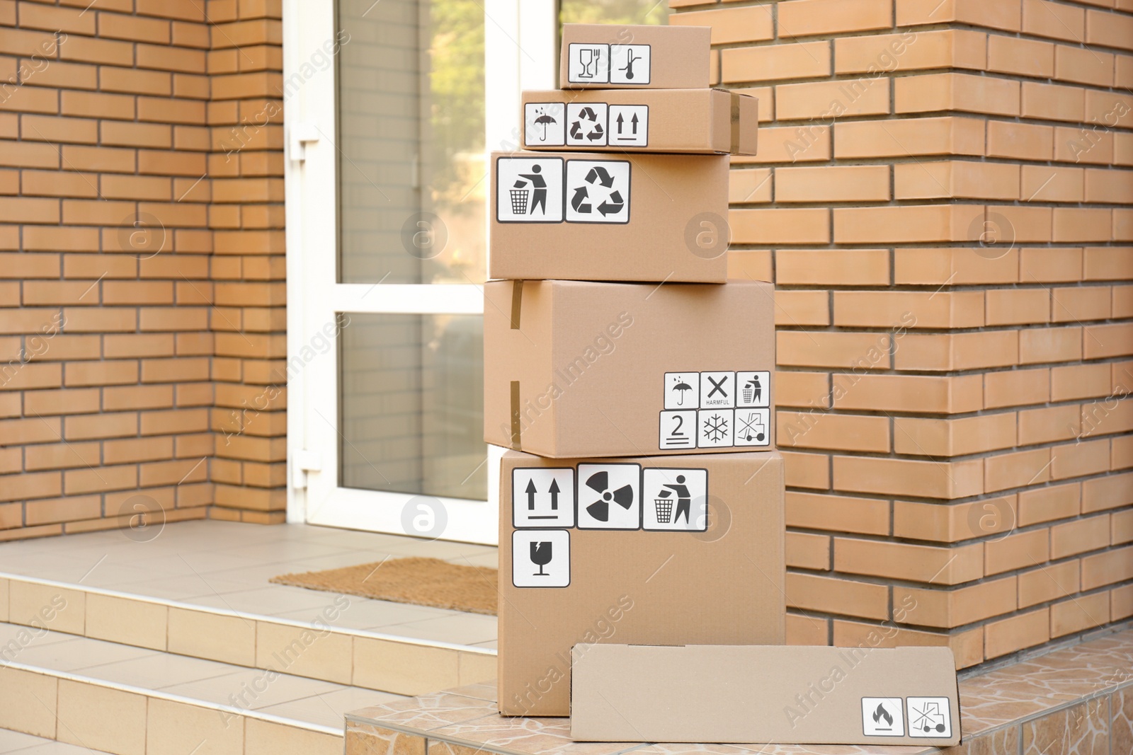 Photo of Cardboard boxes with different packaging symbols on porch near entrance. Parcel delivery