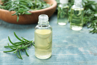 Photo of Fresh rosemary and bottle of essential oil on light blue wooden table. Space for text