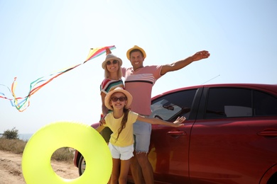 Happy family with inflatable ring and kite near car at beach