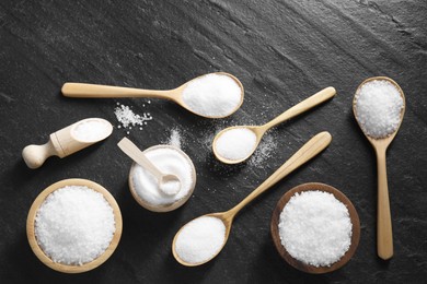 Photo of Organic white salt in bowls and spoons on black table, flat lay