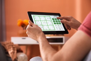 Image of Man playing sudoku game on tablet indoors, closeup