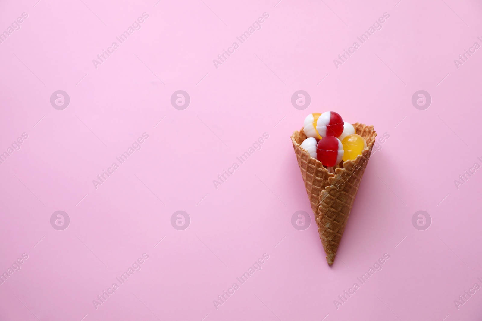 Photo of Delicious lollipop candies in wafer cone on pink background, top view. Space for text